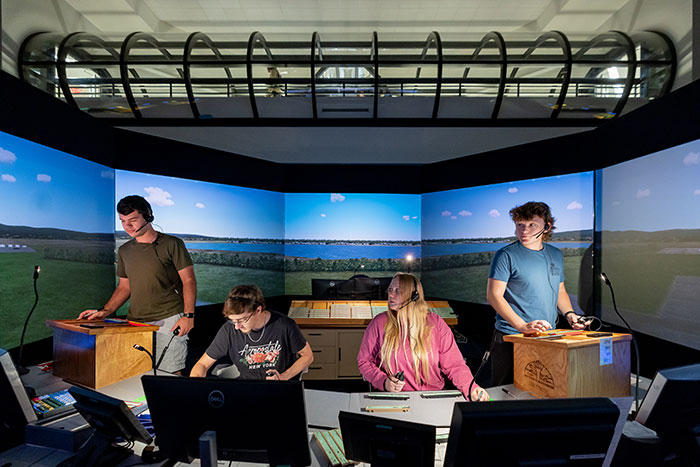 Four students stand in a simulator with screens in 360 degree behind them.