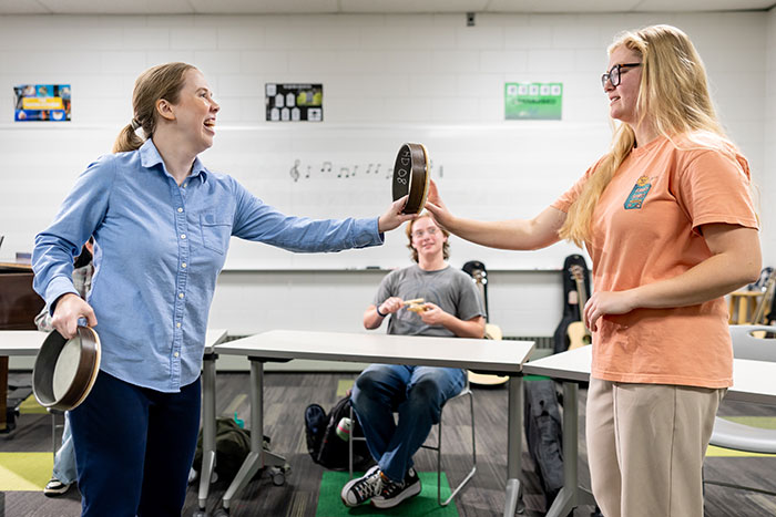 An instructor holds a tambourine up for a student who is reaching for it.