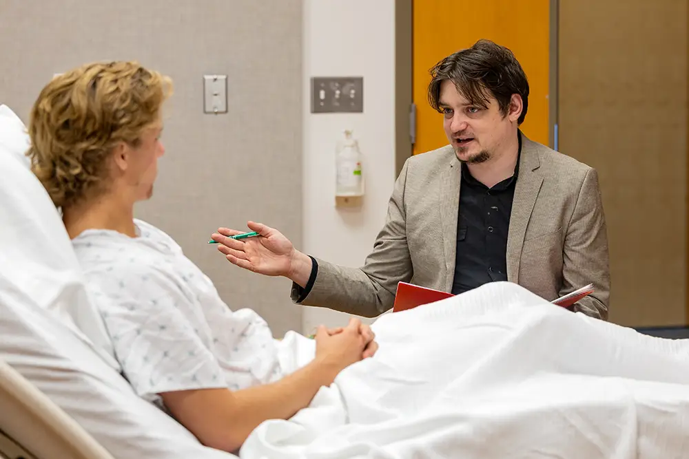 Social work student talking to a patient in a hospital bed