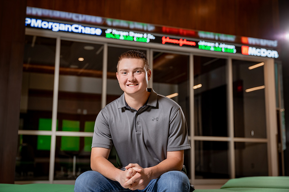 Kaden sitting in front of stock ticker