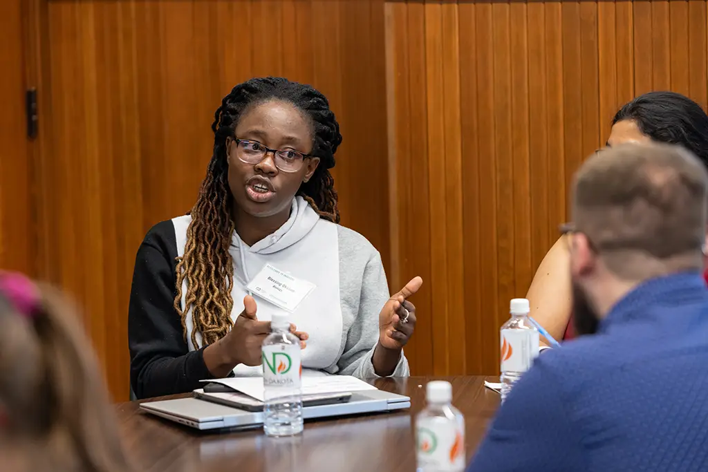 Woman with name tag speaking at a meeting table with laptops and UND branded water bottles