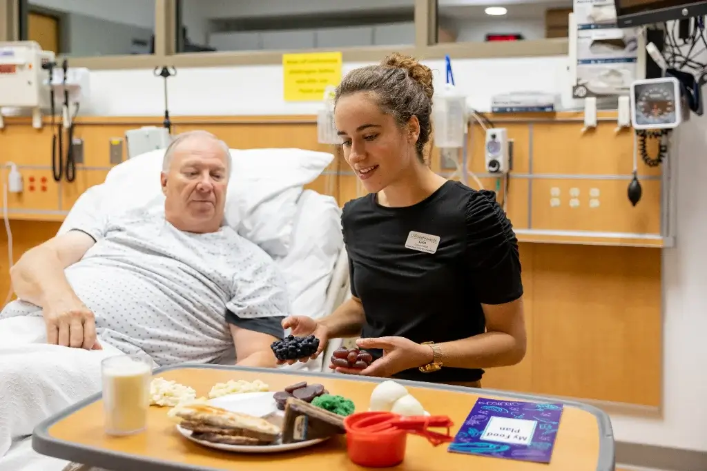 A nutrition student explaining to an elderly patient the nutritional benefits of the food he is going to eat, ensuring it meets his dietary needs