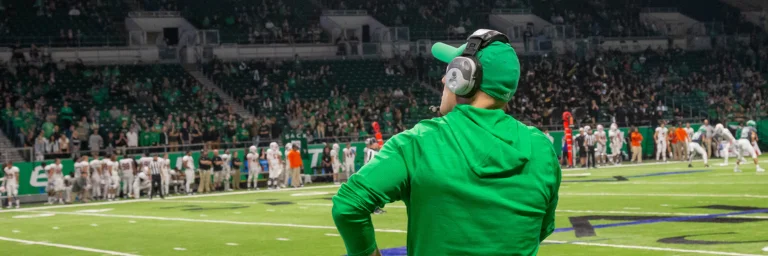 football coach facing away from the camera watching the players on the football field