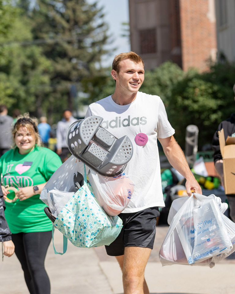 student moving in carrying shower caddy and bags