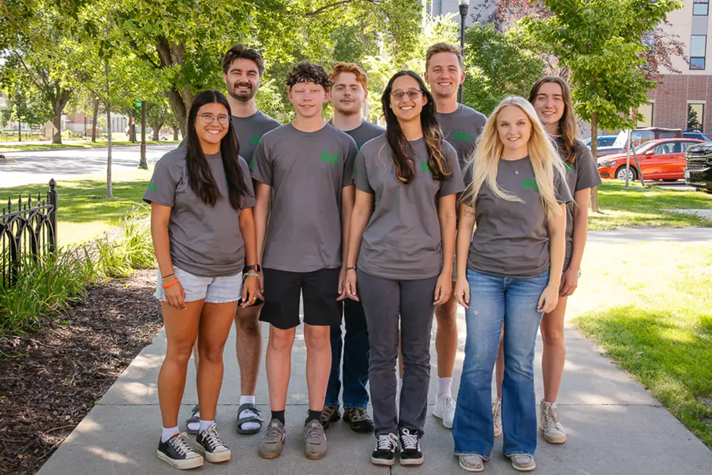 Group of young adults posing for photo with the sidewalk continuing on behind them