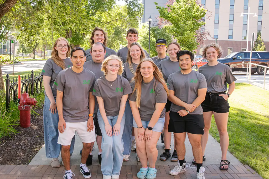 Group of young people pose for a photo with the side walk continuing behind them