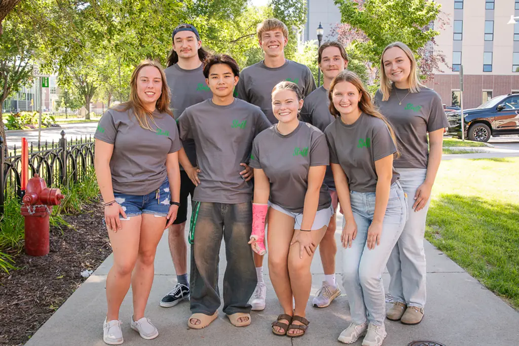 Group of young people pose for a photo with the side walk continuing behind them